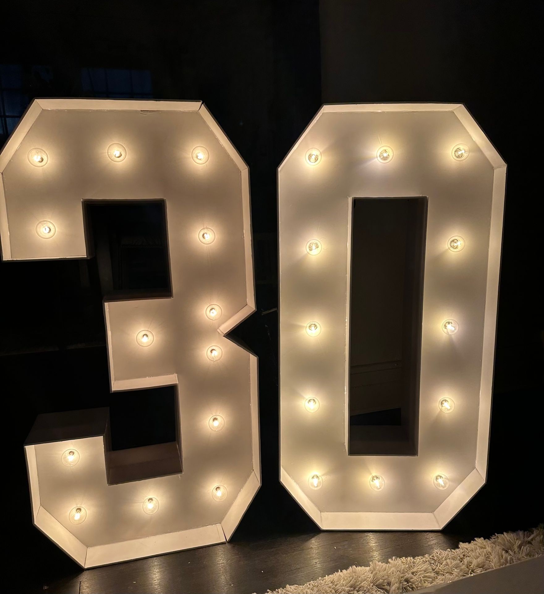 Illuminated marquee lights forming the number 30 against a dark background.