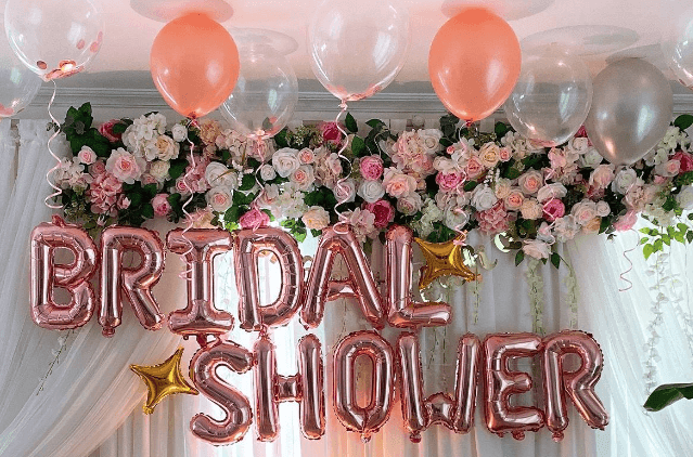 Decorative bridal shower backdrop with rose gold balloon letters, floral arrangements, and assorted balloons.