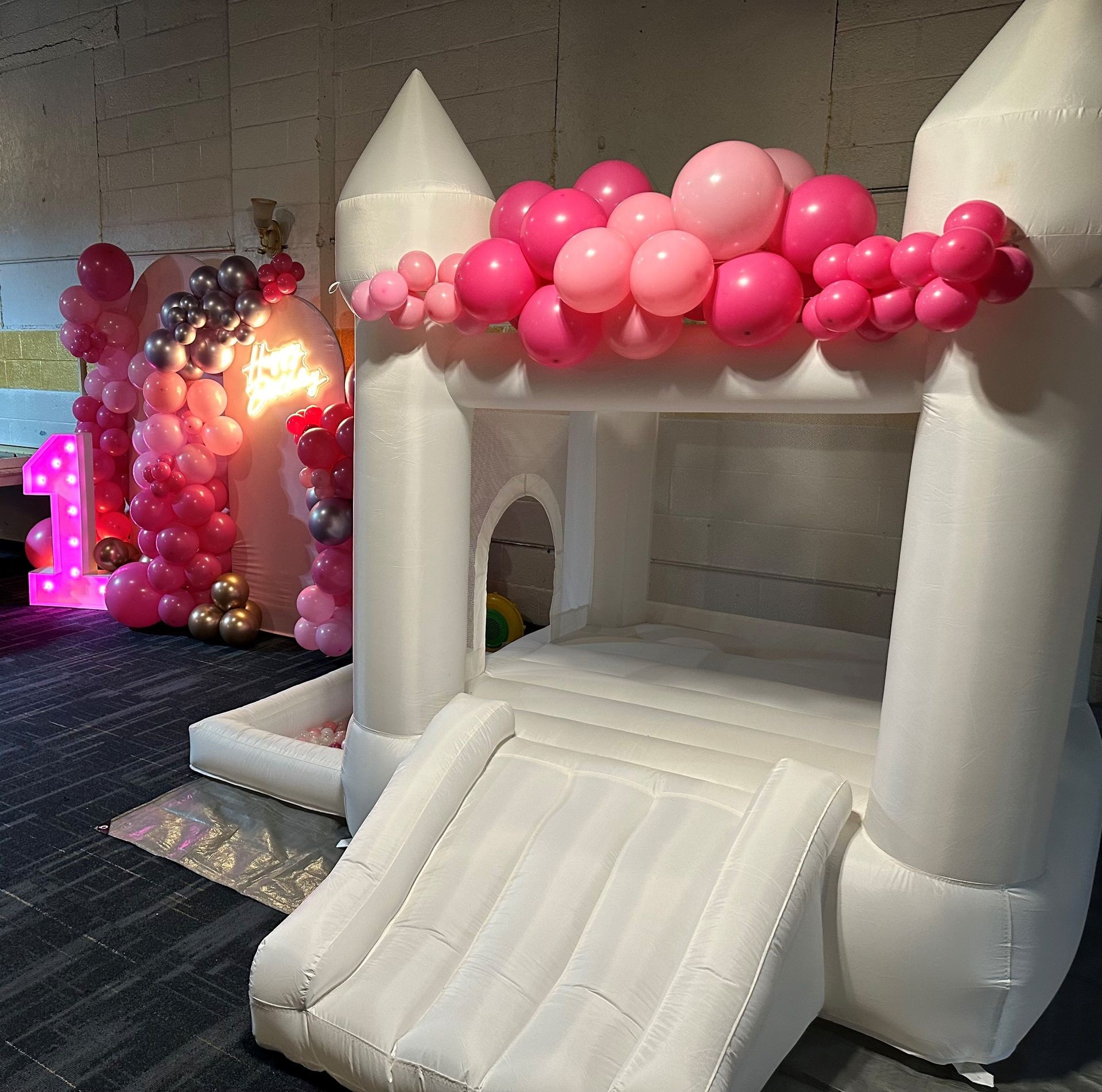 White inflatable castle with pink balloons and lighted number one, set up for a celebration.
