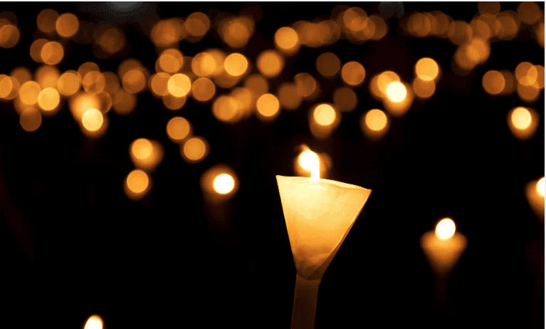 Close-up of a candlelight vigil with numerous lit candles glowing warmly against a dark background.