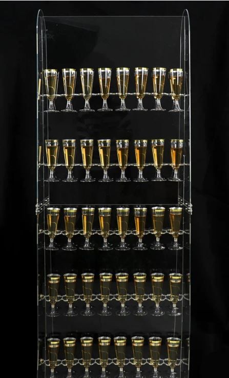 Acrylic shelf with rows of champagne glasses filled with golden liquid against a black background.